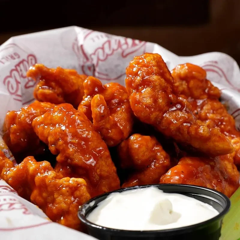 Glossy orange-red boneless chicken wings in a basket with dipping sauce.