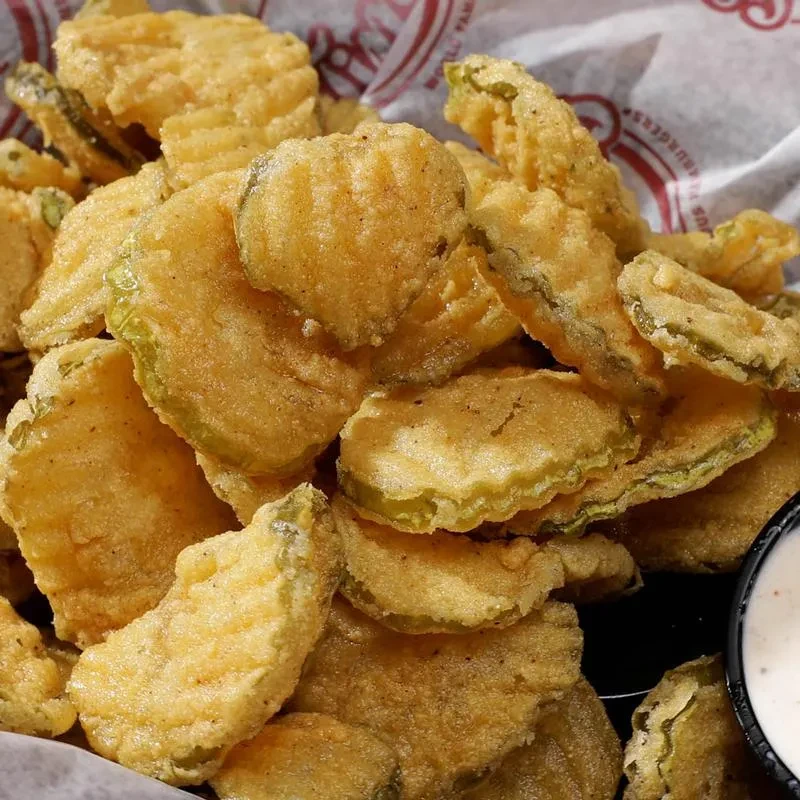 Golden-brown fried pickles piled in a basket with a creamy dipping sauce.