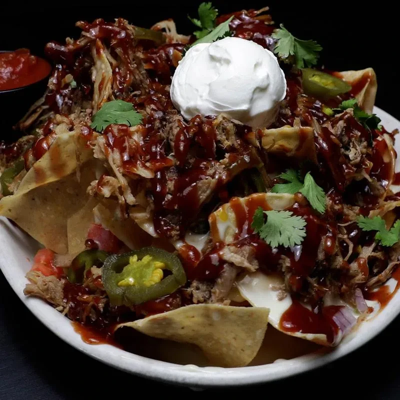 Loaded nachos with shredded BBQ meat, sour cream, and jalapeños.