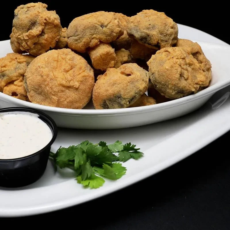 Golden-brown fried mushrooms with dipping sauce and herb garnish.