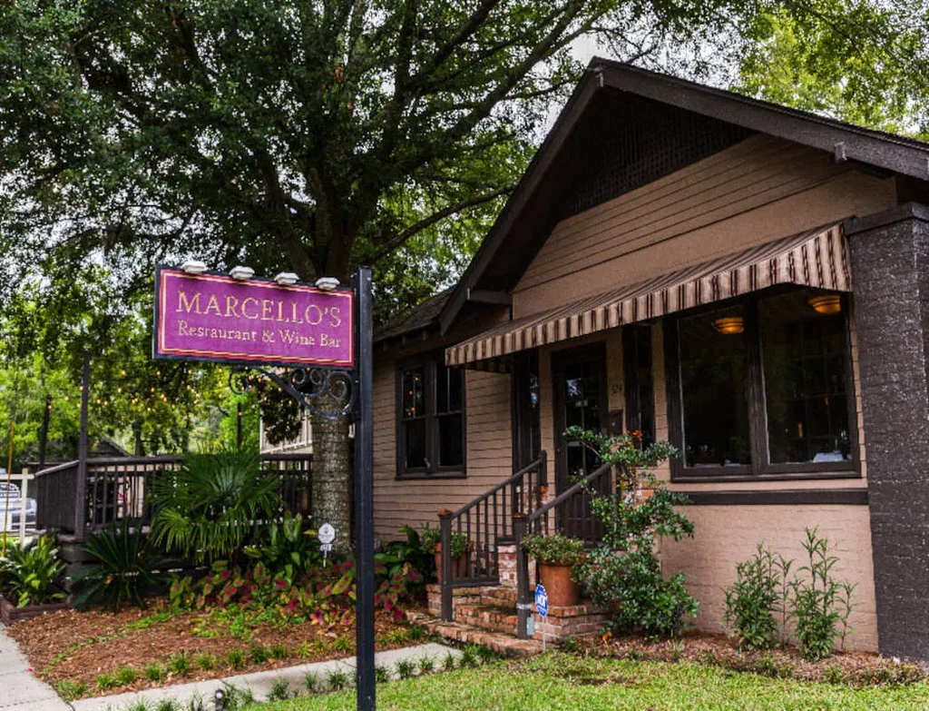 Marcello's Restaurant exterior: brown stucco building, awning, purple sign, landscaping.