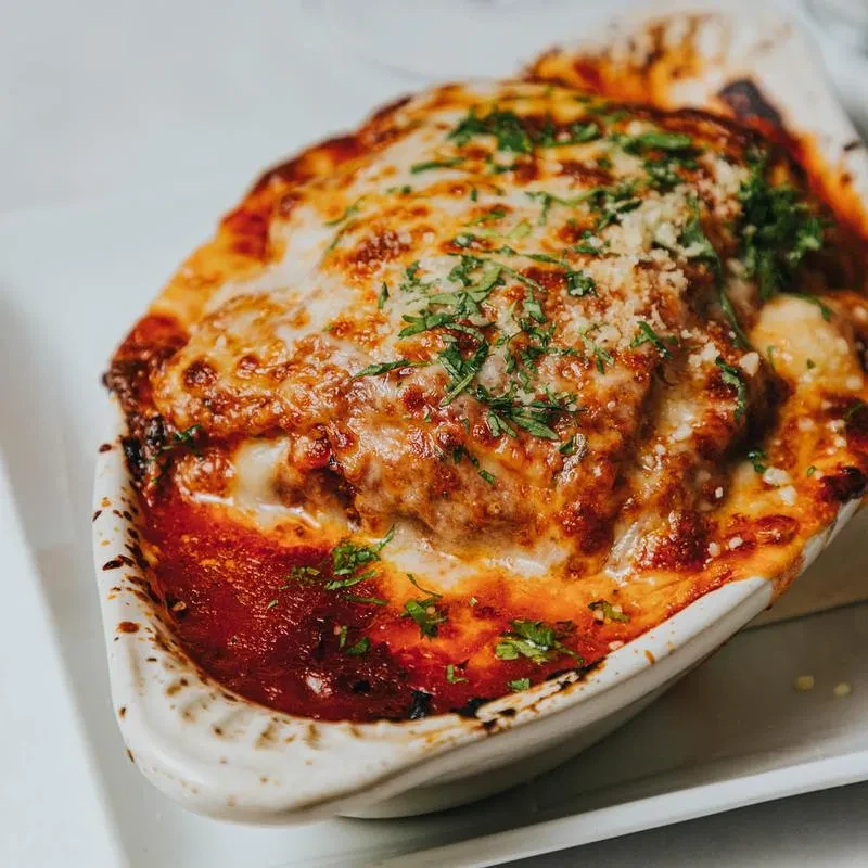 Close-up of bubbling baked pasta with browned cheese, red sauce, and herbs.