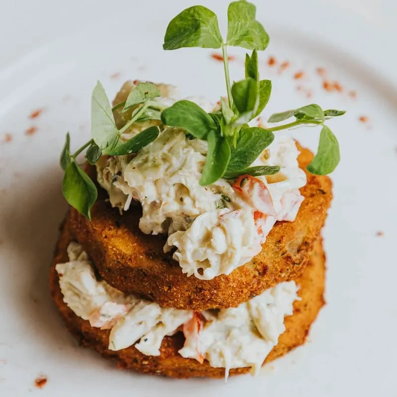 Two stacked fried fritters topped with creamy seafood salad and pea shoots.