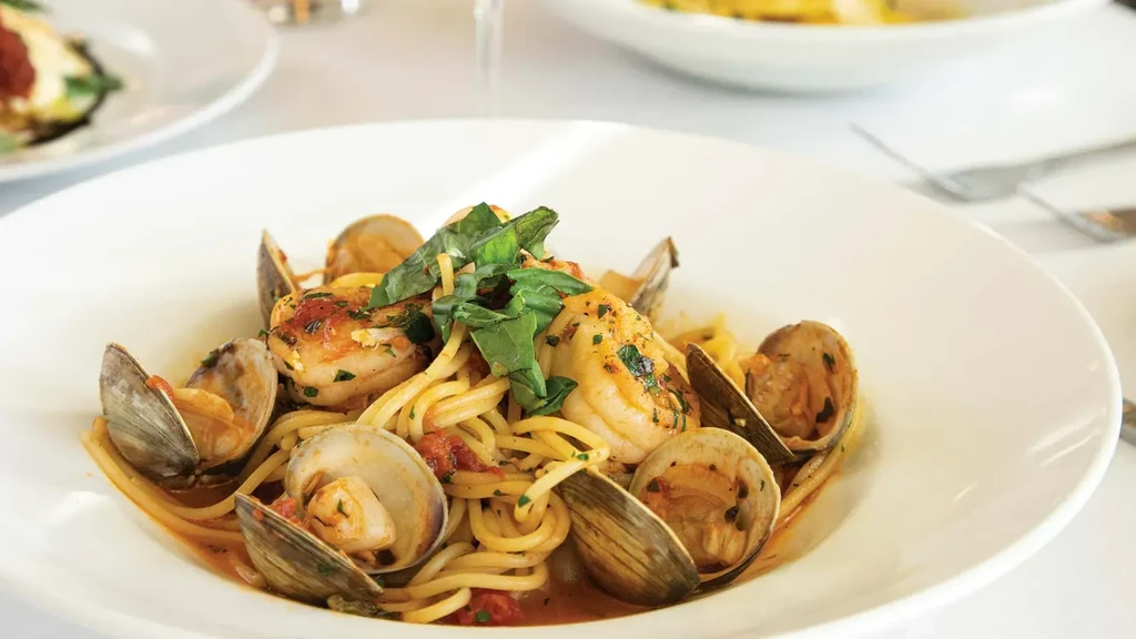 Seafood spaghetti with clams, shrimp, and basil in a white bowl.