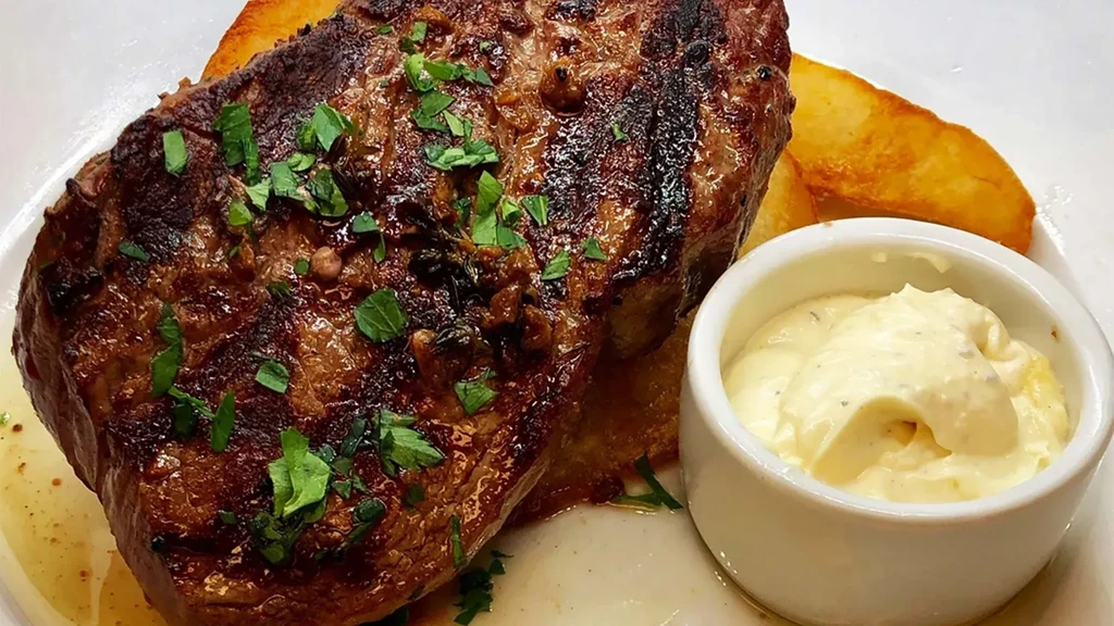 Close-up of seared steak, fresh herbs, potato wedges, and creamy sauce.