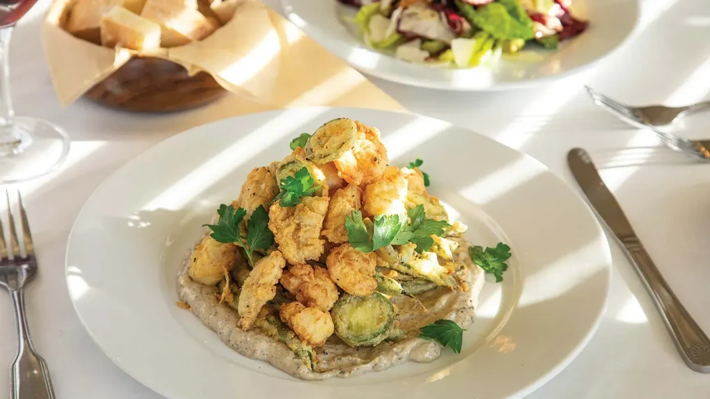 Plate of fried shrimp and vegetables on sauce, garnished with parsley.