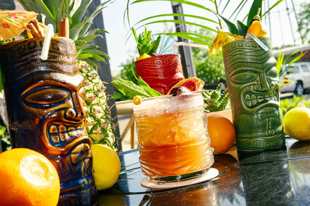 Three garnished tropical cocktails with fruit on a dark table outdoors.