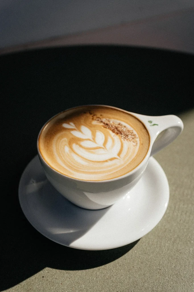 Close-up white cup of latte with rosetta art and cinnamon sprinkle.