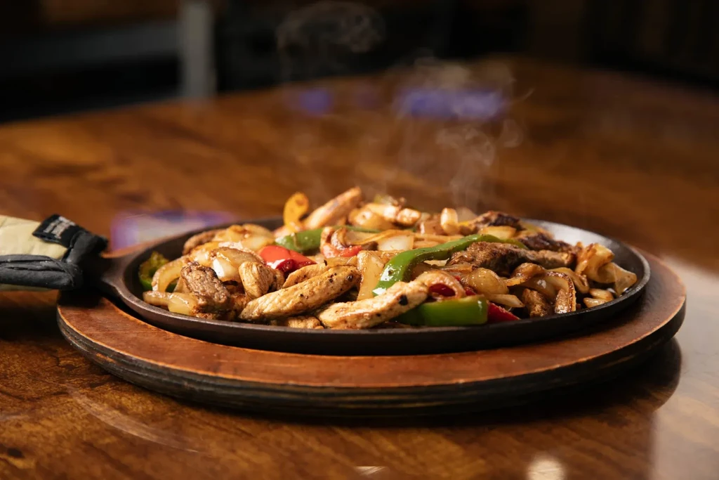 Sizzling chicken and beef fajitas with peppers, onions, in a skillet.