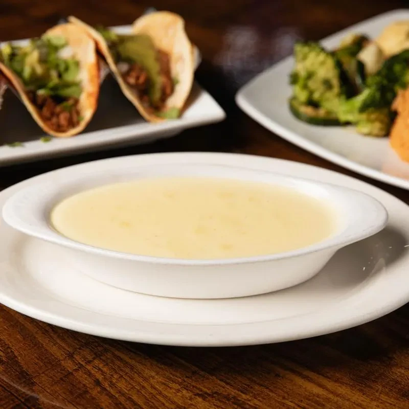 Creamy yellow dip, tacos, and green vegetables on a dark wooden table.