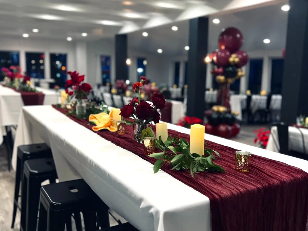 Decorated banquet table with red flowers, candles, and burgundy runner.