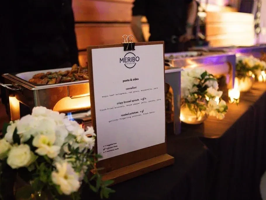 Meribo Catering menu stand at an elegant buffet with chafing dishes.