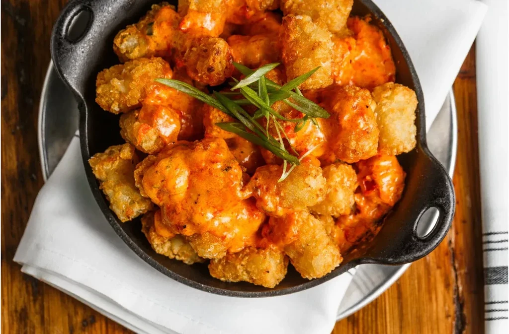 Crispy golden tater tots coated in orange-red sauce and chives.