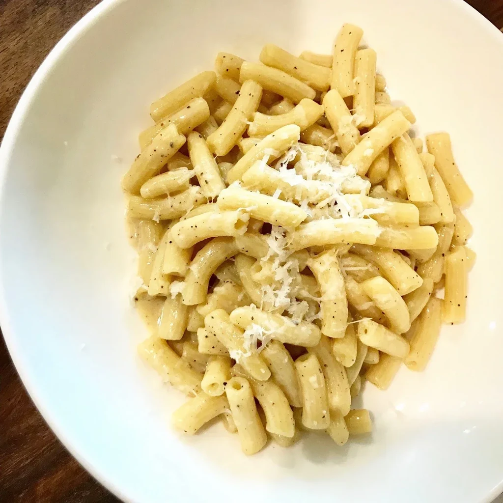 Close-up of rigatoni pasta with creamy sauce, black pepper, and Parmesan.