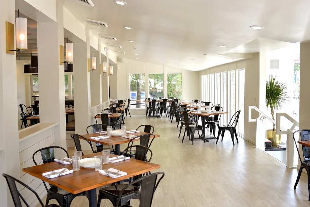 Bright, empty modern restaurant with set tables, large windows, and a staircase.