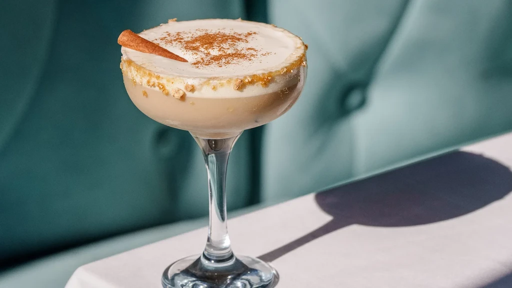 Light beige cocktail with frothy foam, cinnamon, and rim garnish.