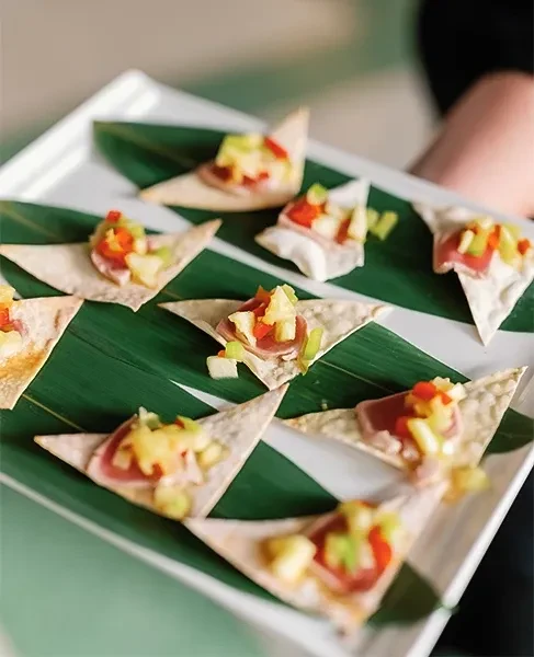 Nine seared tuna appetizers with colorful salsa on a white platter.