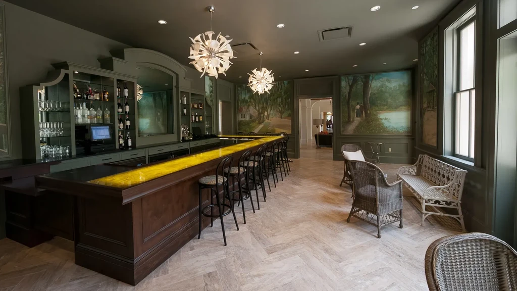 Modern bar with illuminated yellow counter, liquor bottles, and starburst chandeliers.