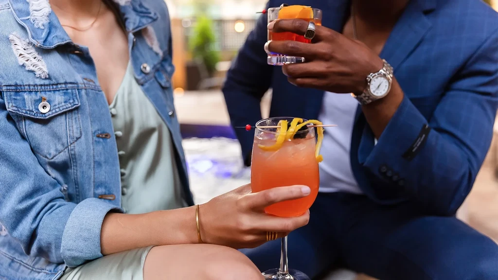 Two people holding garnished cocktails in a relaxed outdoor setting.