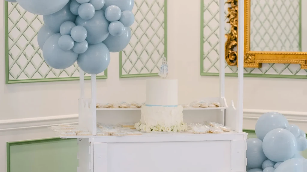Peter Rabbit two-tier cake, cookies, and blue balloons on a white cart.