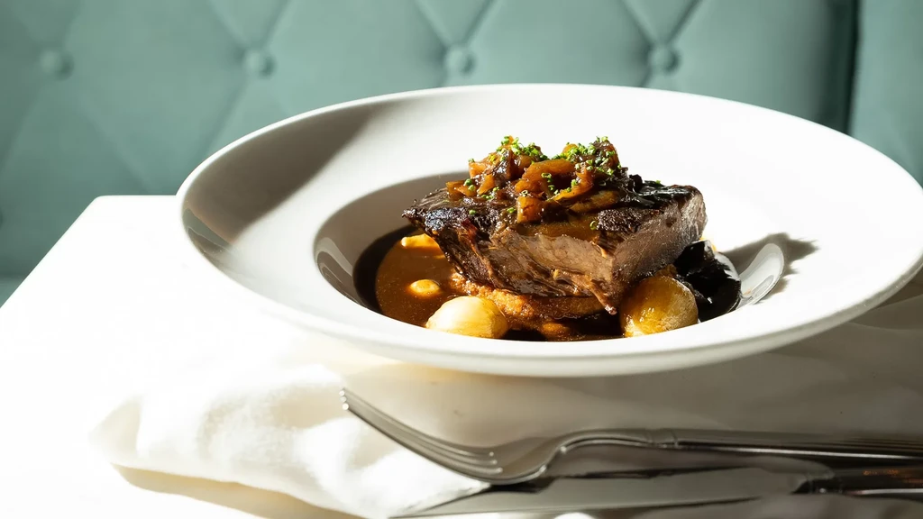 Elegantly plated short rib with caramelized onions, creamy base, and rich dark sauce.