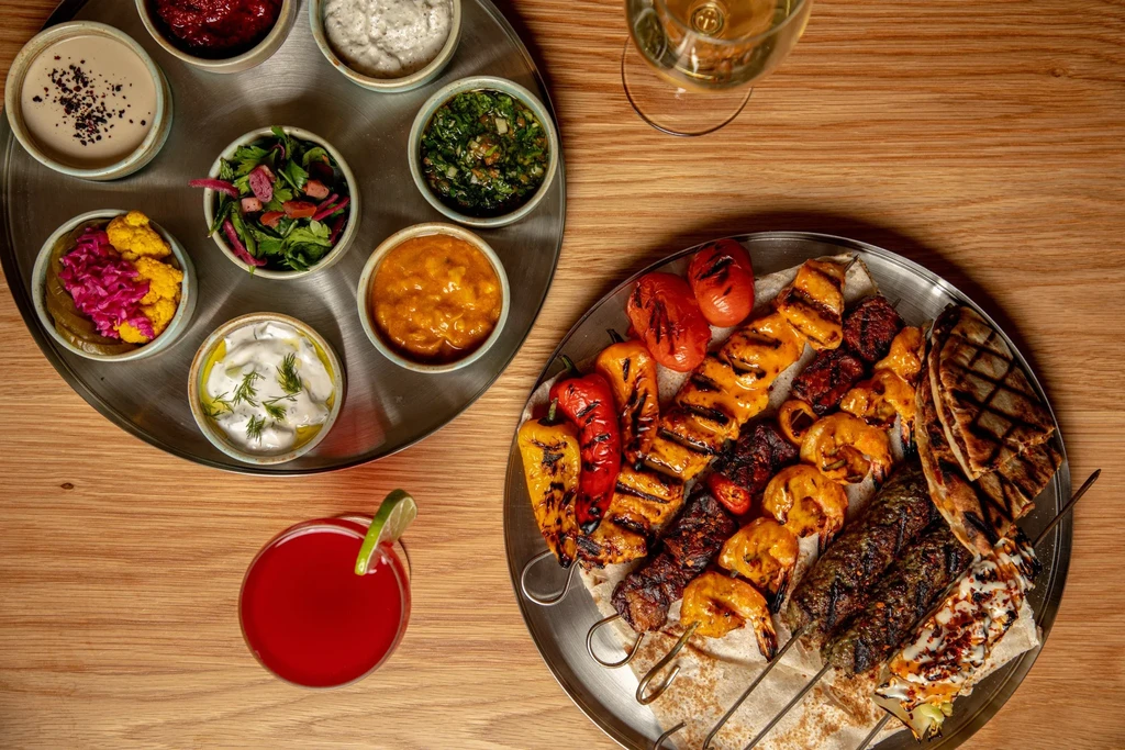 Overhead shot: elaborate spread of grilled skewers, dips, salads, and drinks.