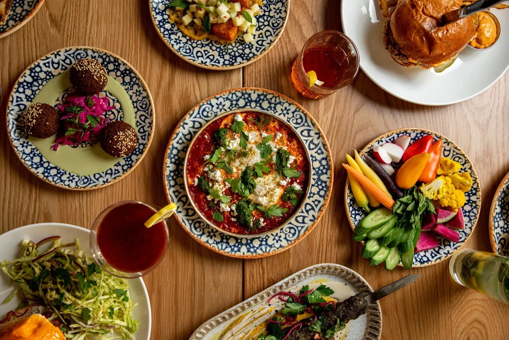 Flat lay of falafel, stew, burger, and drinks on a table.