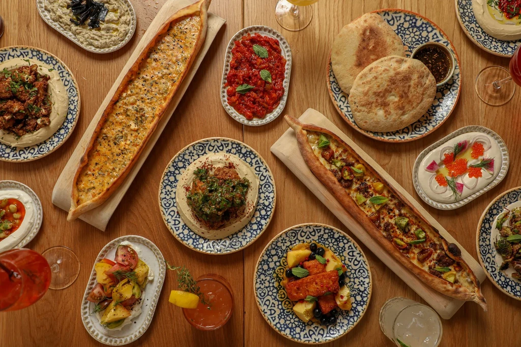 Wooden table laden with Middle Eastern flatbreads, dips, salads, and drinks.