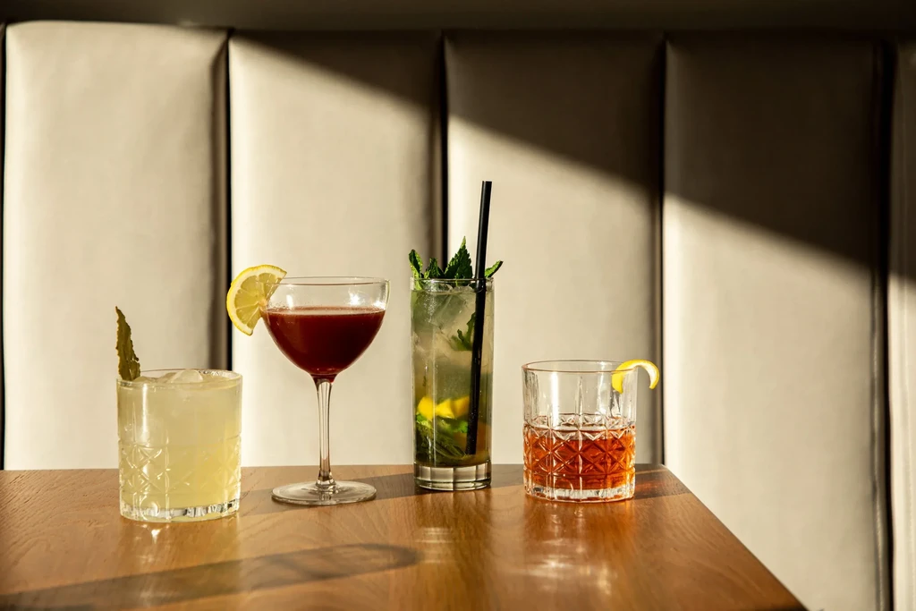 Four distinct, garnished cocktails on a polished wooden table.