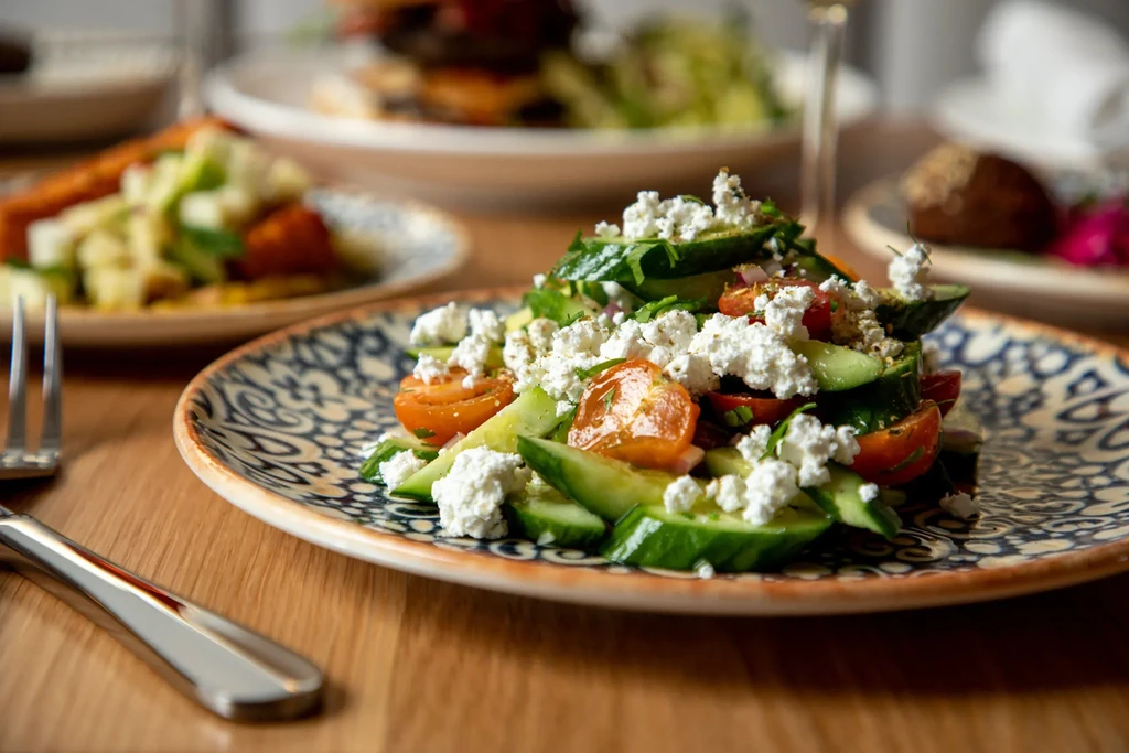 Close-up of fresh salad with cucumbers, tomatoes, and crumbled white cheese.