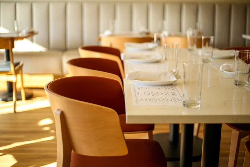Long, light-colored restaurant table with modern chairs, set for dining.
