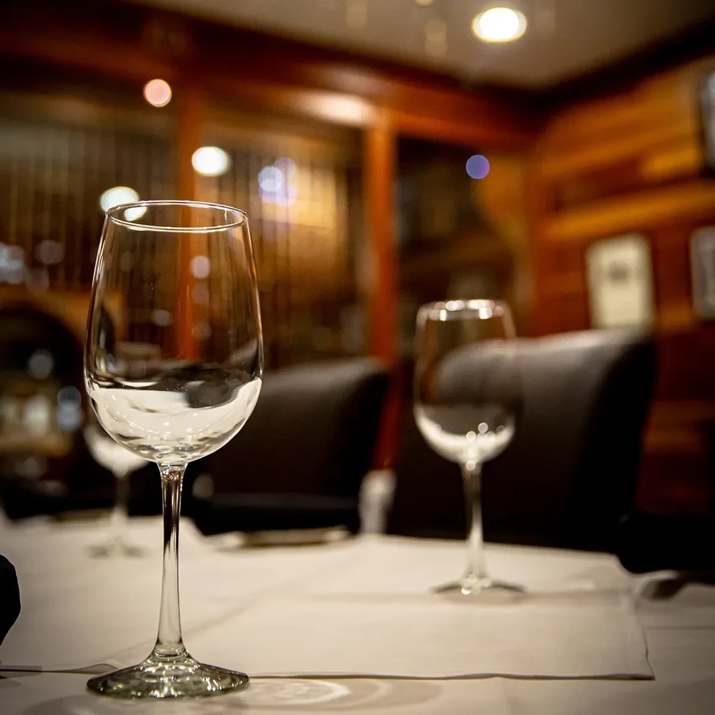 Empty wine glass on table in dimly lit, wood-paneled restaurant.