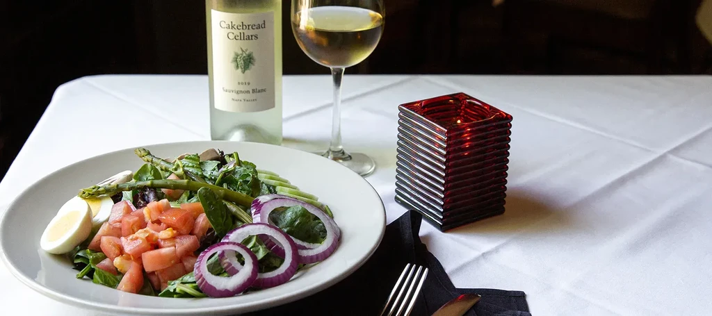 Plate of fresh salad with wine bottle, glass, and lit candle.
