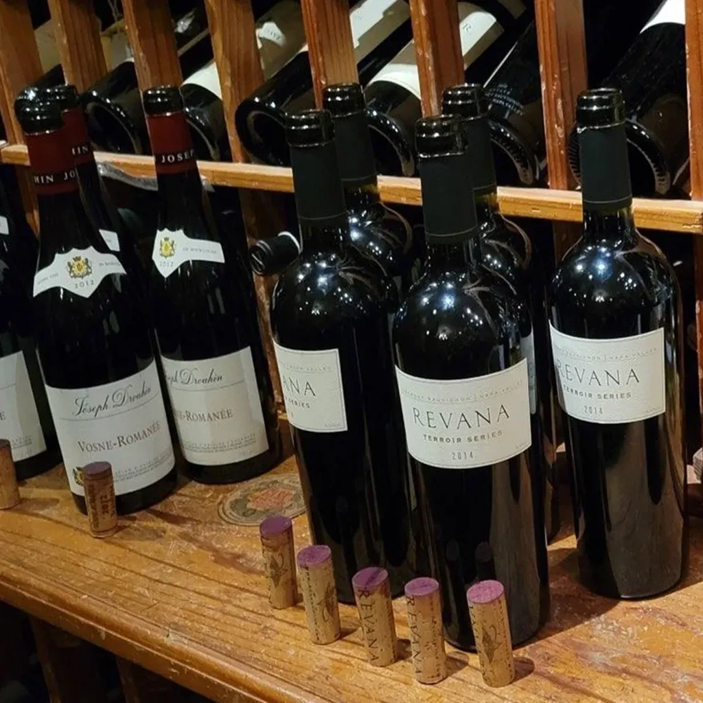 Close-up of Joseph Drouhin and Revana wine bottles on rustic wooden shelf.