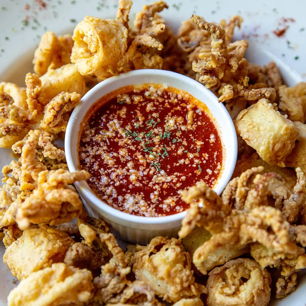 Golden-brown fried calamari with red marinara sauce on a plate.