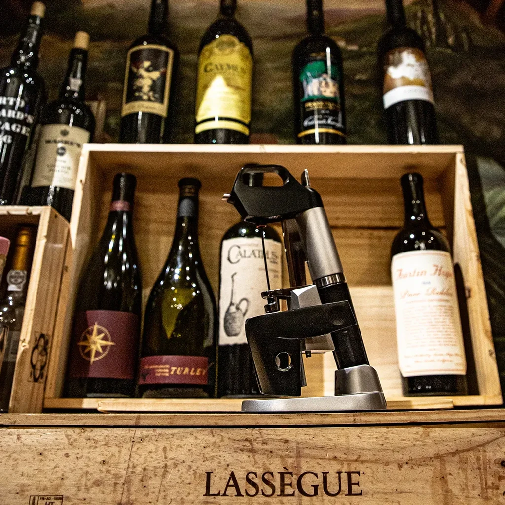 A sleek wine preservation system sits on a crate amidst wine bottles.