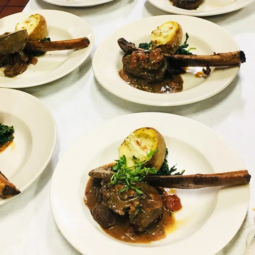 Multiple plates of stewed meat, potatoes, and greens in a kitchen.