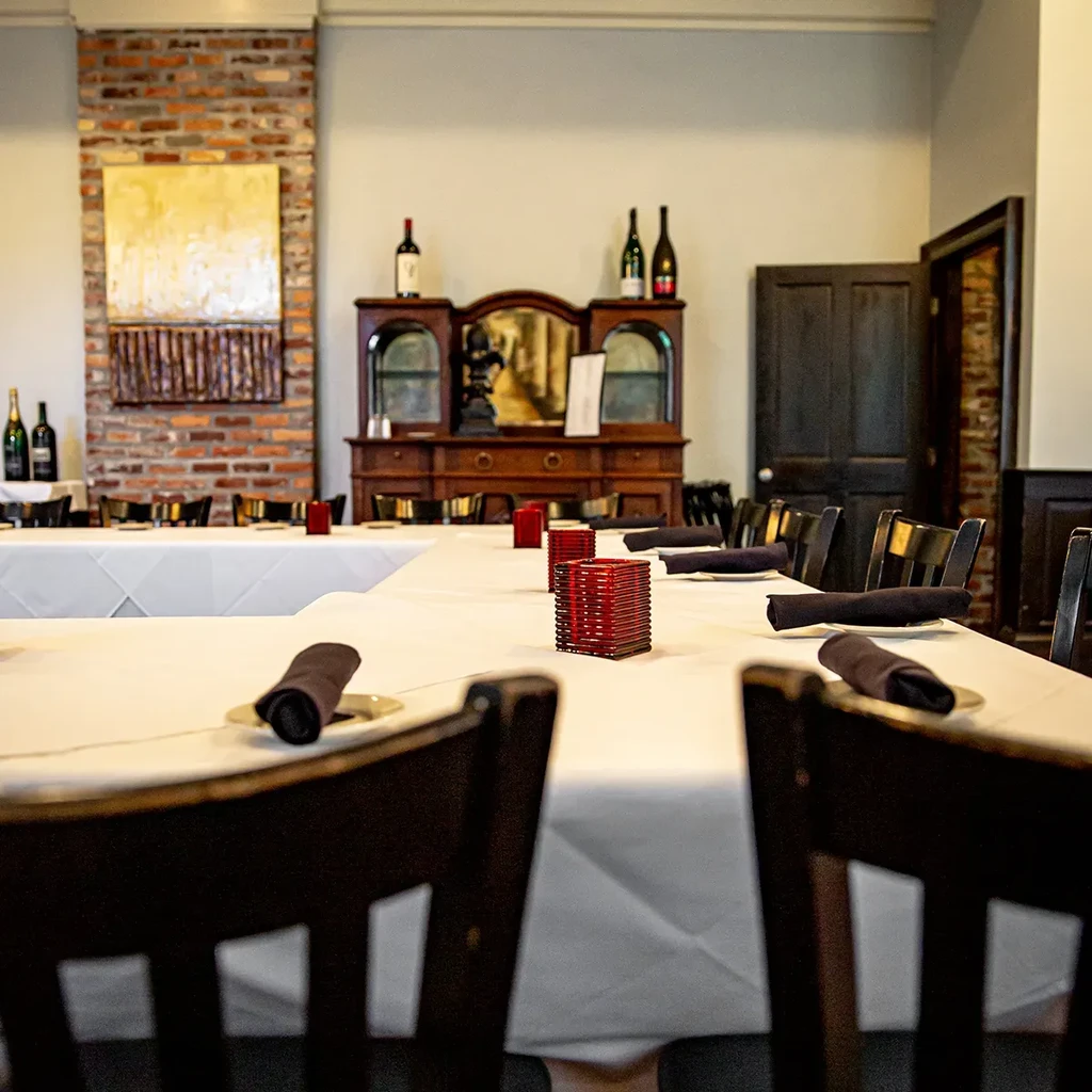 Restaurant dining room with set tables, brick wall, and wine hutch.