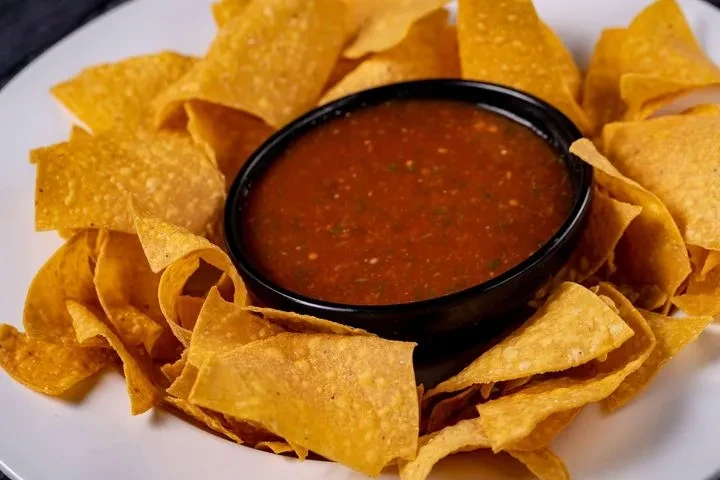 Black bowl of chunky red salsa surrounded by golden tortilla chips.