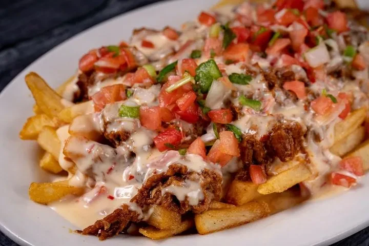 Close-up of loaded fries topped with cheese, meat, and pico de gallo.