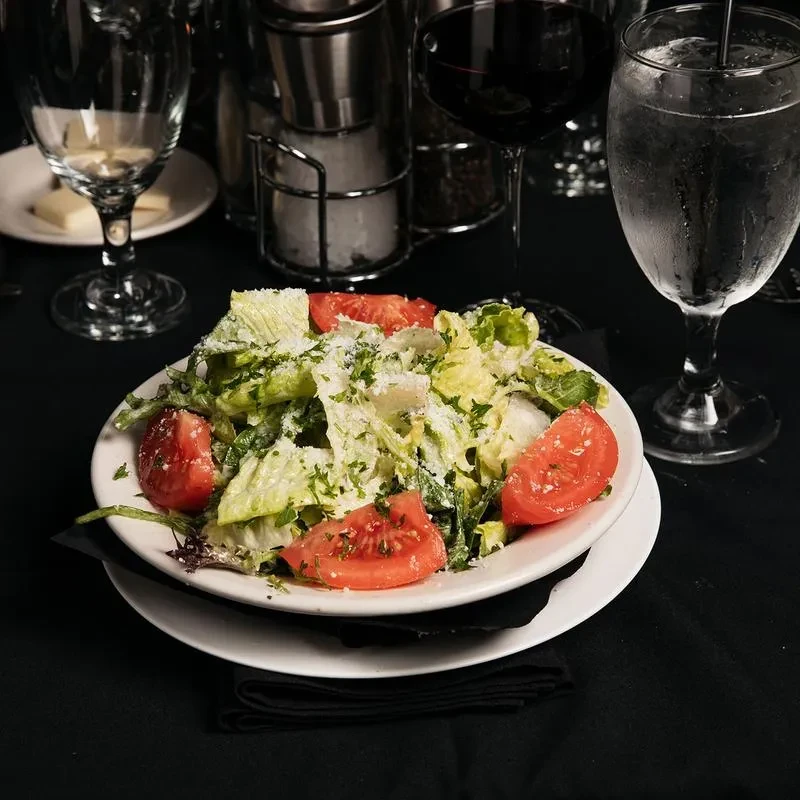 Fresh salad with lettuce, tomatoes, cheese, and herbs in a white bowl.