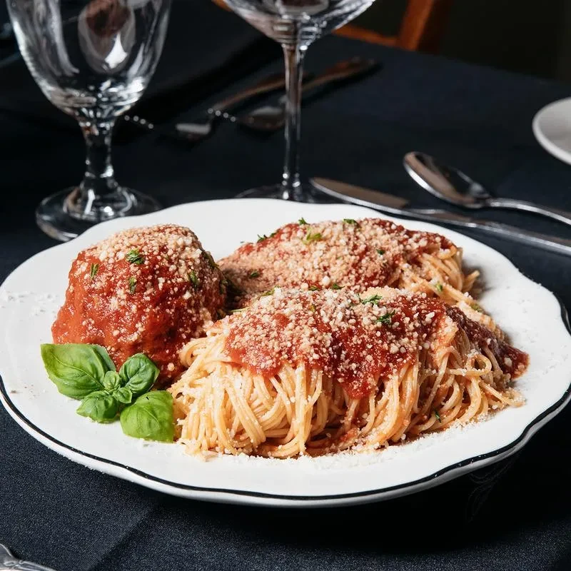 Spaghetti and meatballs with red sauce, cheese, and herbs on a white plate.