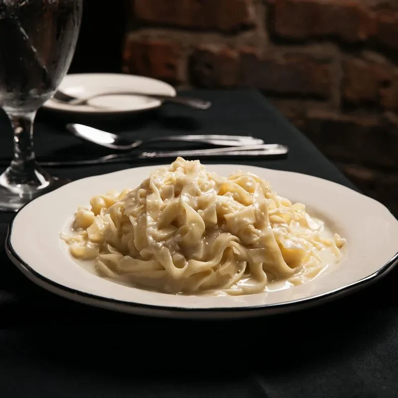 Creamy pasta on a white plate with water and silverware.