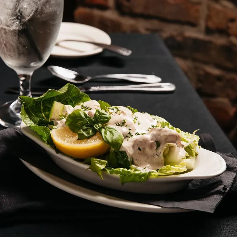 Fresh green salad with creamy dressing, basil, and lemon in a white dish.