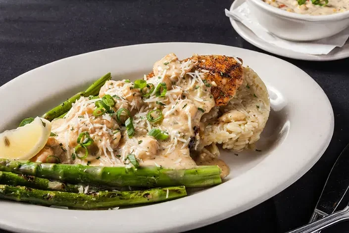 Plated grilled protein, creamy sauce, rice, charred asparagus, lemon.