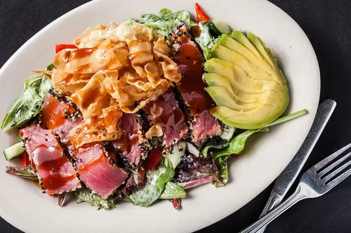 Plated seared tuna salad with avocado, wontons, and greens.