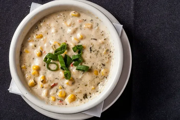 Overhead creamy corn chowder, garnished with scallions, in a white bowl.