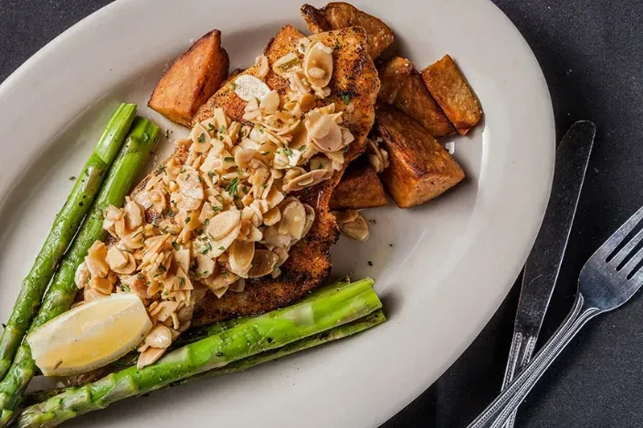 Plated grilled fish with almonds, asparagus, roasted potatoes, and lemon.
