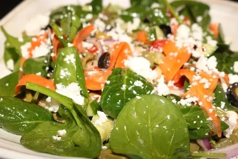 Close-up of colorful salad with spinach, carrots, olives, cucumber, feta cheese.