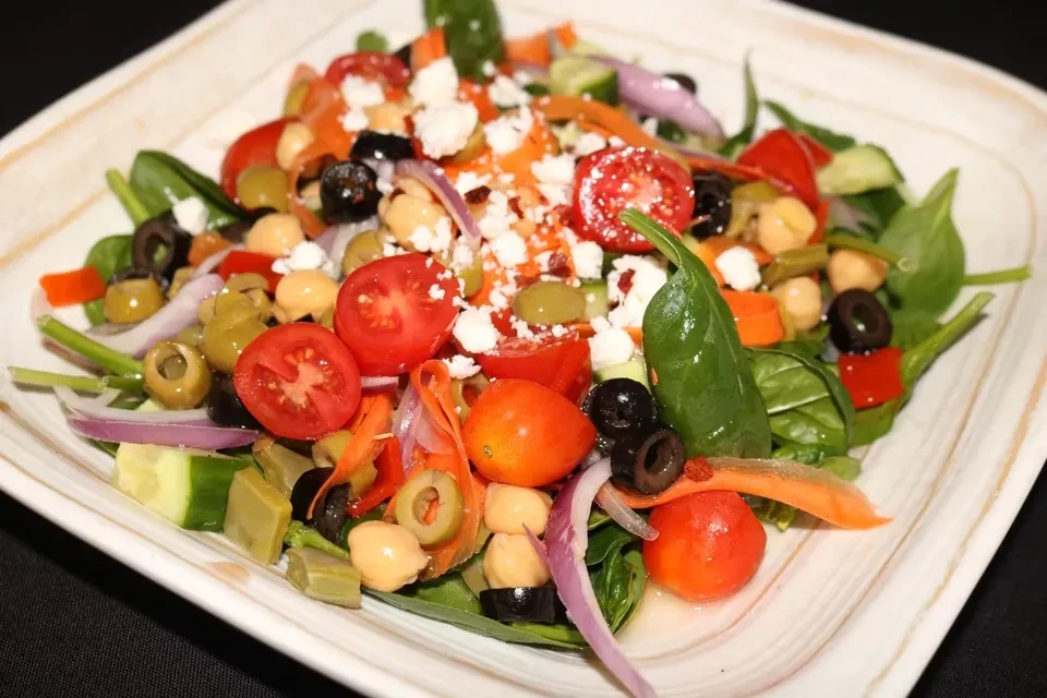 Colorful salad with vegetables, feta, and vinaigrette in a white bowl.